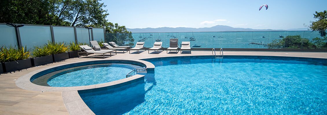 Piscina com espreguiçadeiras e vista para o mar e montanhas ao fundo, ideal para lazer e relaxamento em um ambiente de alto padrão.