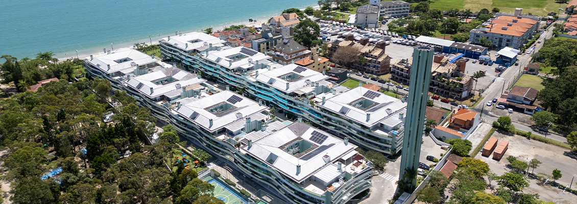 Imagem aérea de um condomínio de luxo à beira-mar, com várias torres residenciais modernas cercadas por áreas verdes e acesso à praia, em uma cidade costeira.