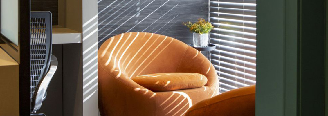 Imagem de um espaço de trabalho moderno com cadeira de escritório e uma poltrona confortável na esquina, com iluminação natural e decoração minimalista.