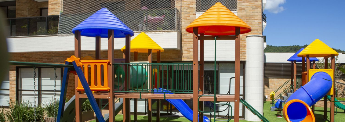 Parque infantil em área externa com brinquedos coloridos, incluindo escorregadores em formato de cone azul, vermelho e amarelo, além de torre e corrimões
